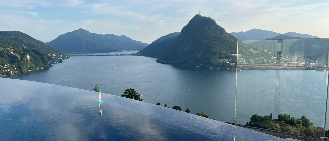 An infinity pool on a terrace above a lake, with a mountain rising from the shore
