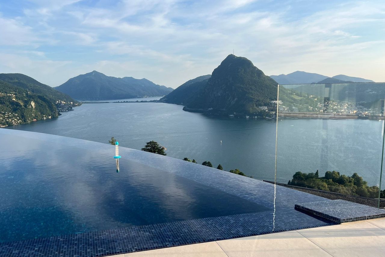 An infinity pool on a terrace above a lake, with a mountain rising from the shore