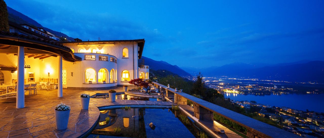 The terrace of a villa at dusk, above a lake and the lights of the town