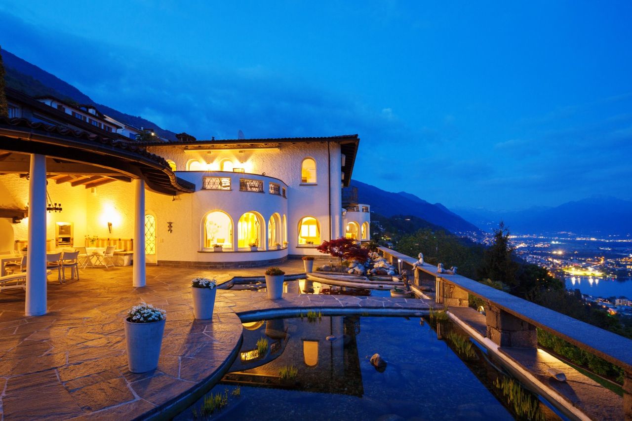 The terrace of a villa at dusk, above a lake and the lights of the town